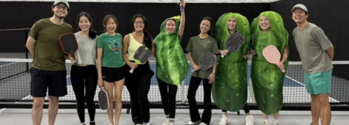 Velocity members on an indoor pickleball court, two wearing pickle costumes